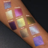 Top angled arm swatches on medium skin tone of Witchcraft vs. Alchemy Collection including Calx Duochrome Eyeshadow next to Wormwood, Sol, Cinnabar, Crucible, Rune, Elixir, Arcana, Aqua Fortis