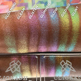 Straight angled arm swatches on deep skin tone of Gilding Glitter-Type Iridescent Multichrome Eyeshadow compared to Gloaming, Gleam, Glisten, Glimmer, Glow, Glint