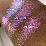 Close up right angled arm swatches on deep skin tone of Glimmer Glitter-Type Iridescent Multichrome Eyeshadow shifts compared to Glow, Glisten