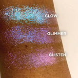 Close up top angled arm swatches on deep skin tone of Glimmer Glitter-Type Iridescent Multichrome Eyeshadow shifts compared to Glow, Glisten