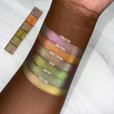 Top angled arm swatches on deep skin tone of Iron Gate Earth Vibrant Multichrome Eyeshadow shifts compared to Cobblestone, Royal Peach, Bronze Fountain, Estate and Royal Pear