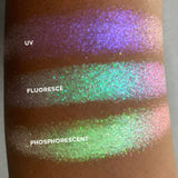 Close up arm swatches on medium skin tone of Phosphorescent Iridescent Multichrome Eyeshadow shifts compared to UV, Fluoresce