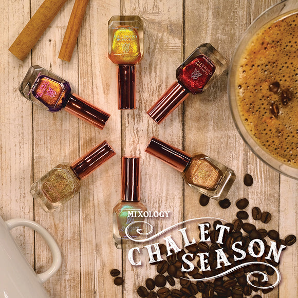 Six nail polish bottles laid out on wood grain background, with coffee beans, mug and cinnamon stick around.
