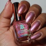 Close-up shot of Cosmopolitan nail lacquer applied to finger nails on a darker skin tone, with nail lacquer bottle in hand
