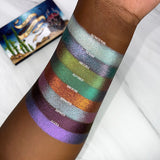 Arm swatches on deep skin tone of all 8 shadows included in the Deep Sea Treasures Palette with the palette in the background. 