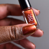 Close up shot of thumb painted with Ring of Fire on deep skin tone holding the Mini Nail Lacquer bottle