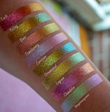 Bottom left angled arm swatches on fair skin tone of Engrave Glitter Multichrome Eyeshadow shifts compared to Torch, Foiling, Blaze, Translucency, Corrosion, Ornamental, Chandelier