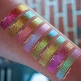 Bottom left angled arm swatches on fair skin tone of Chandelier Glitter Multichrome Eyeshadow shifts compared to Torch, Foiling, Blaze, Translucency, Corrosion, Ornamental, Engrave