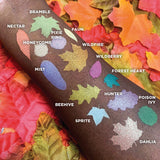 Top angled leaf arm swatches on deep skin tone of The Woodlands Collection including Dahlia Duochrome Eyeshadow next to Mist, Hunter, Pixie Ring, Wildfire, Honeycomb, Forest Heart, Beehive